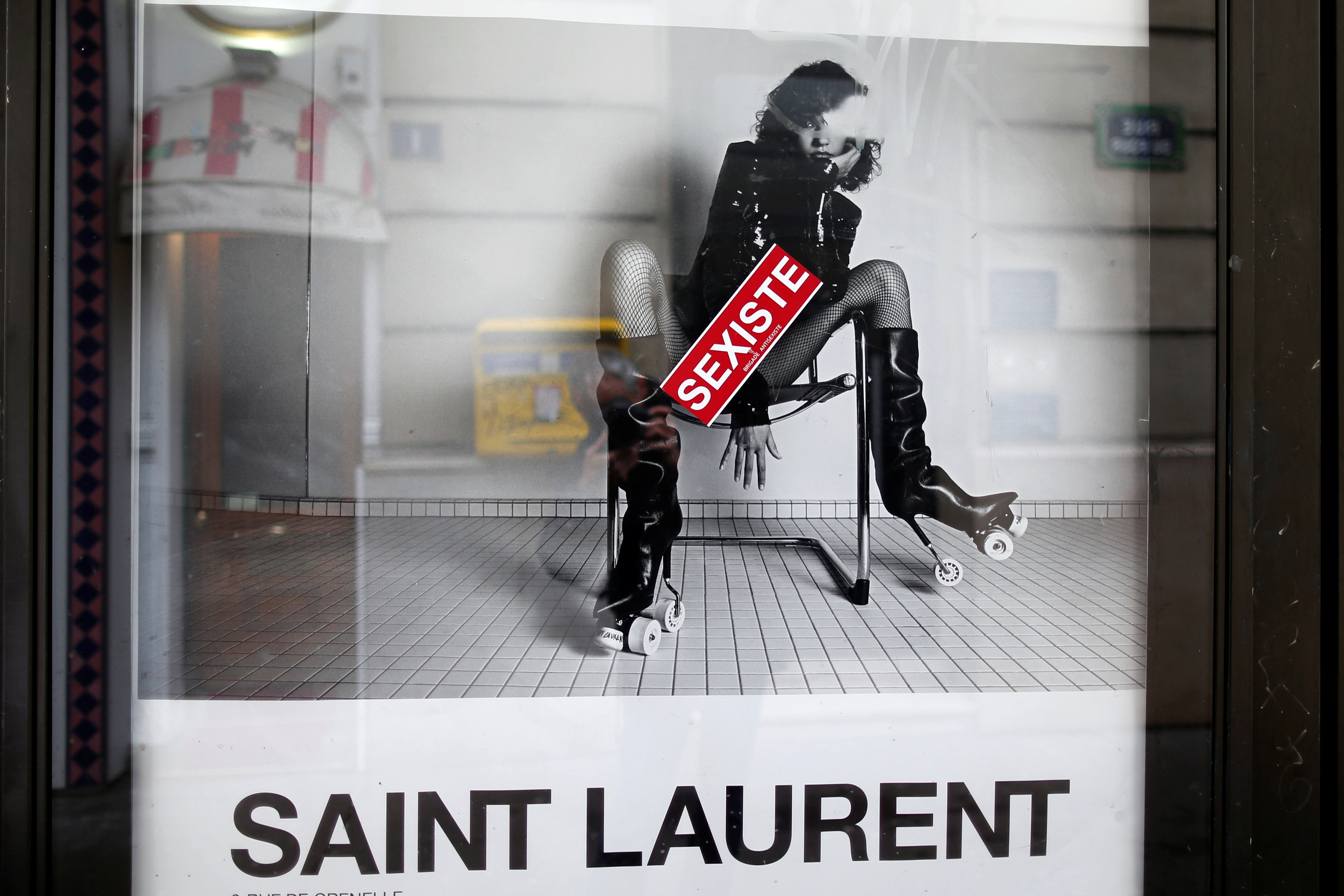 A sticker which reads "sexist" is seen on an ad by French fashion house Yves Saint Laurent displayed on a newspaper kiosk in Paris