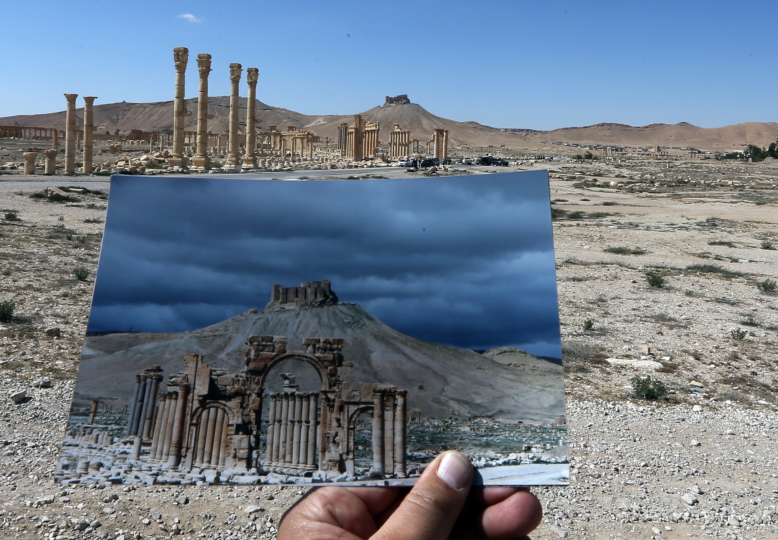 A general view taken on March 31, 2016 shows a photographer holding his picture of the Arc du Triomphe (Triumph's Arch) taken on March 14, 2014 in front of the remains of the historic monument after it was destroyed by Islamic State (IS) group jihadists in October 2015 in the ancient Syrian city of Palmyra.
Syrian troops backed by Russian forces recaptured Palmyra on March 27, 2016, after a fierce offensive to rescue the city from jihadists who view the UNESCO-listed site's magnificent ruins as idolatrous.

 / AFP / JOSEPH EID        (Photo credit should read JOSEPH EID/AFP/Getty Images)