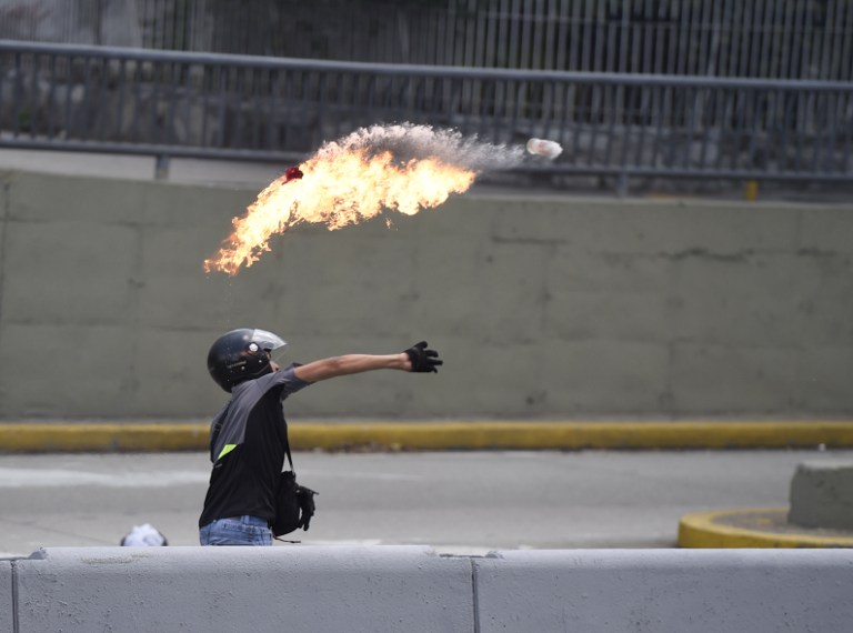 A demonstrator against Nicolas Maduro's government throws a Molotov cocktail during clashes with riot police at eastern Caracas on April 8, 2017.  The opposition is accusing pro-Maduro Supreme Court judges of attempting an internal "coup d'etat" for attempting to take over the opposition-majority legislature's powers last week. The socialist president's supporters held counter-demonstrations on Thursday, condemning Maduro's opponents as "imperialists" plotting with the United States to oust him.  / AFP PHOTO / JUAN BARRETO