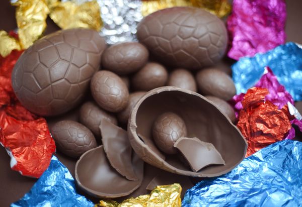 Opened chocolate Easter Eggs in a pile amongst their colourful foil wrappers with one large egg broken in half