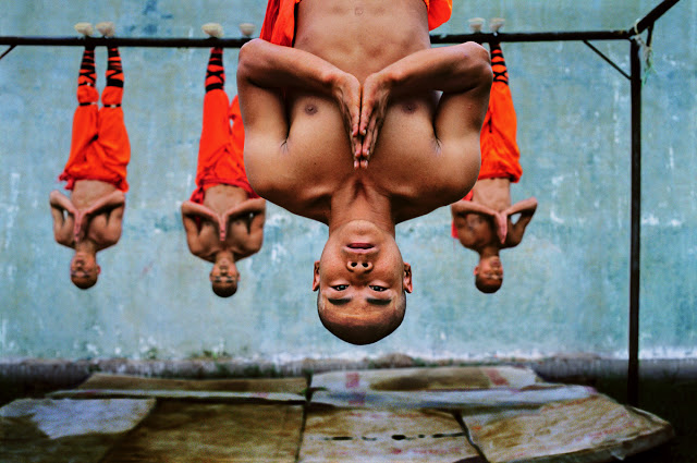 Shaolin monks training, Zhengzhou, China, 2004..The world famous Shaolin Monastery is known to many in the West for its association with martial arts, specifically Shaolin Kung Fu. McCurry pictures the monks suspended from a metal beam. The physical strength and dexterity displayed by the monks is incredible, although they exude a deep serenity...Phaidon..Iconic_Book..final print_UrbanArt'12.final print_MACRO'11