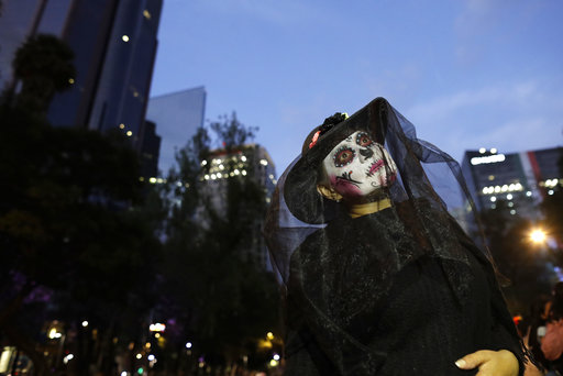 A woman dressed as Mexico's iconic "Catrina" poses for a picture during the Grand Procession of the Catrinas, part of upcoming Day of the Dead celebrations in Mexico City, Sunday, Oct. 22, 2017. The figure of a skeleton wearing an elegant broad-brimmed hat was first done as a satirical engraving by artist Jose Guadalupe Posada sometime between 1910 and his death in 1913. (AP Photo/Rebecca Blackwell)