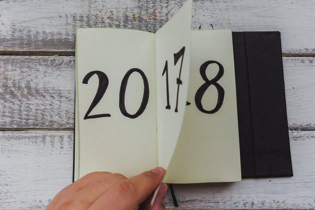 Man flips notepad sheet on white wooden table. 2017 is turning, 2018 is opening, top view