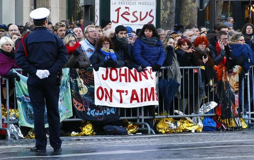 Fans show a banner reading "Johnny, we love you" for late French rock star Johnny Hallyday before his funeral ceremony in Paris, Saturday, Dec.9, 2017. France is bidding farewell to its biggest rock star, honoring Johnny Hallyday with an exceptional funeral procession down the Champs-Elysees, a presidential speech and a motorcycle parade, all under intense security. (AP Photo/Francois Mori)