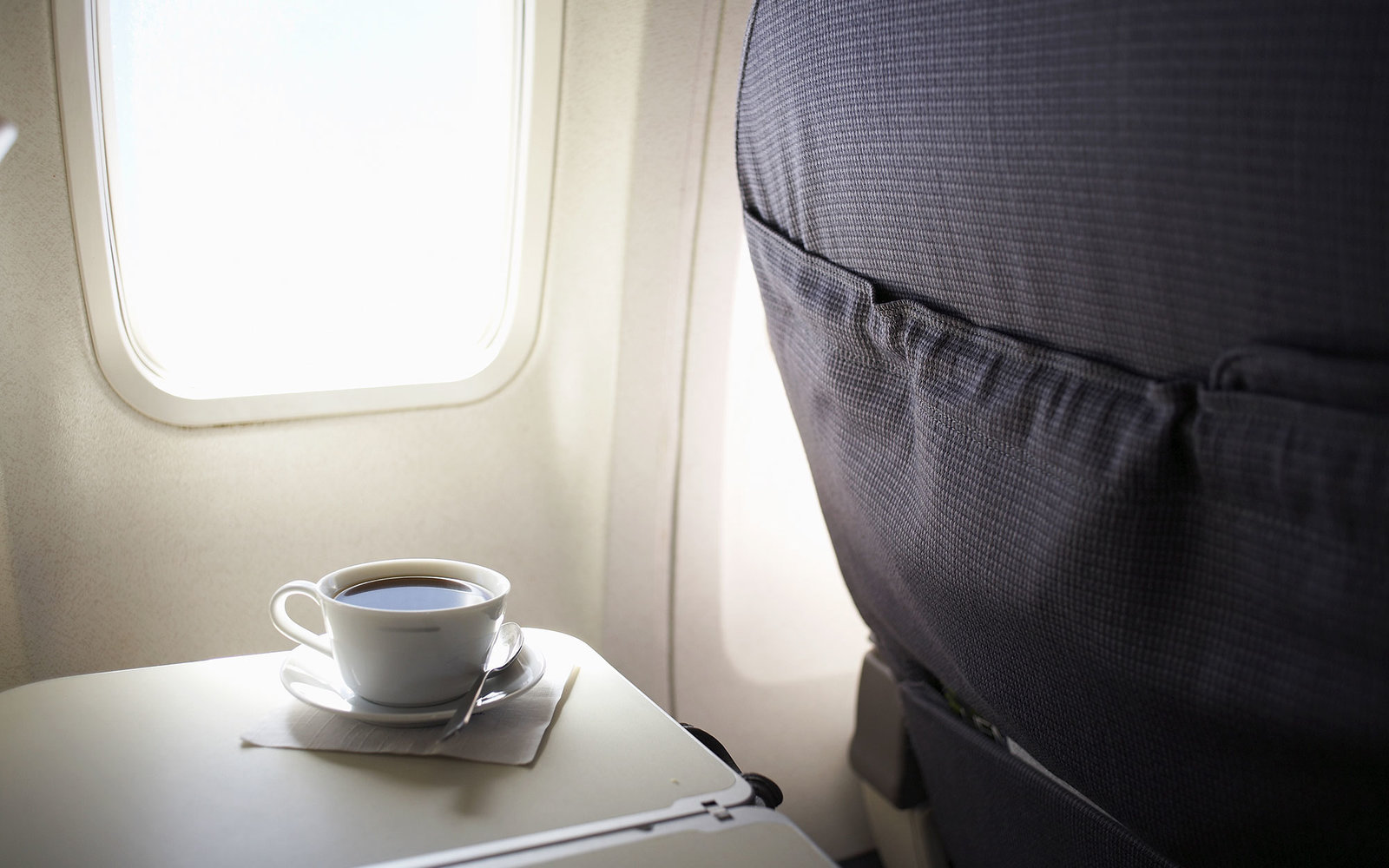 Cup of coffee on airplane tray table by window, elevated view