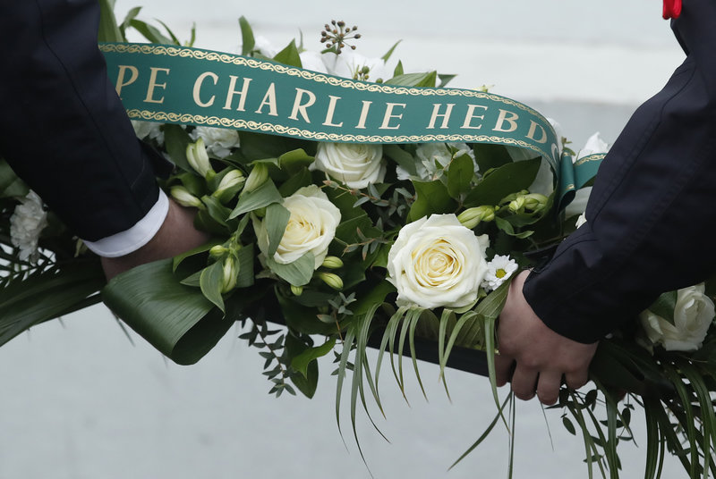 French police officers hold a wreath of flowers before a ceremony outside the kosher grocery where Amedy Coulibaly killed four people, during the third anniversary of the attack, in Paris, Sunday, Jan. 7, 2018. Macron paid respects to the 17 people killed when Islamic extremists attacked satirical newspaper Charlie Hebdo and a kosher supermarket three years ago, in the first of several attacks to rock France. (Christian Hartmann/Pool via AP)