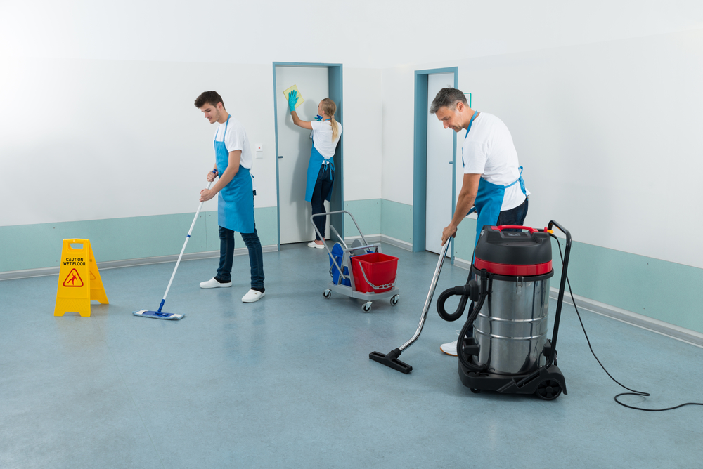 Group Of Janitors Cleaning Corridor With Cleaning Equipments