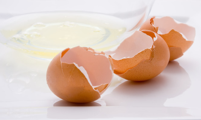 Three broken eggs and a bowl with egg white