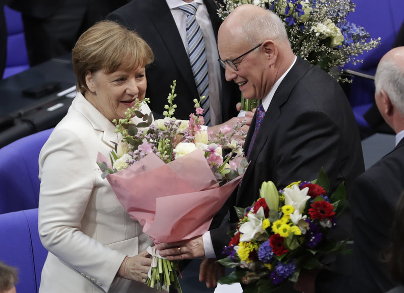 German Chancellor Angela Merkel receives flowers by Christian Democratic parties faction leader Volker Kauder after she has been elected for a fourth term as chancellor in Berlin, Germany, Wednesday, March 14, 2018. (AP Photo/Michael Sohn)