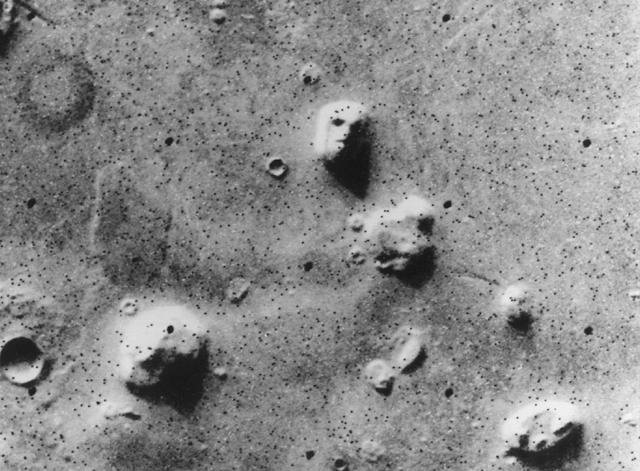 NASA's Viking 1 Orbiter spacecraft photographed this region in the northern latitudes of Mars on July 25, 1976 while searching for a landing site for the Viking 2 Lander. The speckled appearance of the image is due to missing data, called bit errors, caused by problems in transmission of the photographic data from Mars to Earth. Bit errors comprise part of one of the 'eyes' and 'nostrils' on the eroded rock that resembles a human face near the center of the image. Shadows in the rock formation give the illusion of a nose and mouth. Planetary geologists attribute the origin of the formation to purely natural processes. The feature is 1.5 kilometers (one mile) across, with the sun angle at approximately 20 degrees. The picture was taken from a range of 1,873 kilometers (1,162 miles).