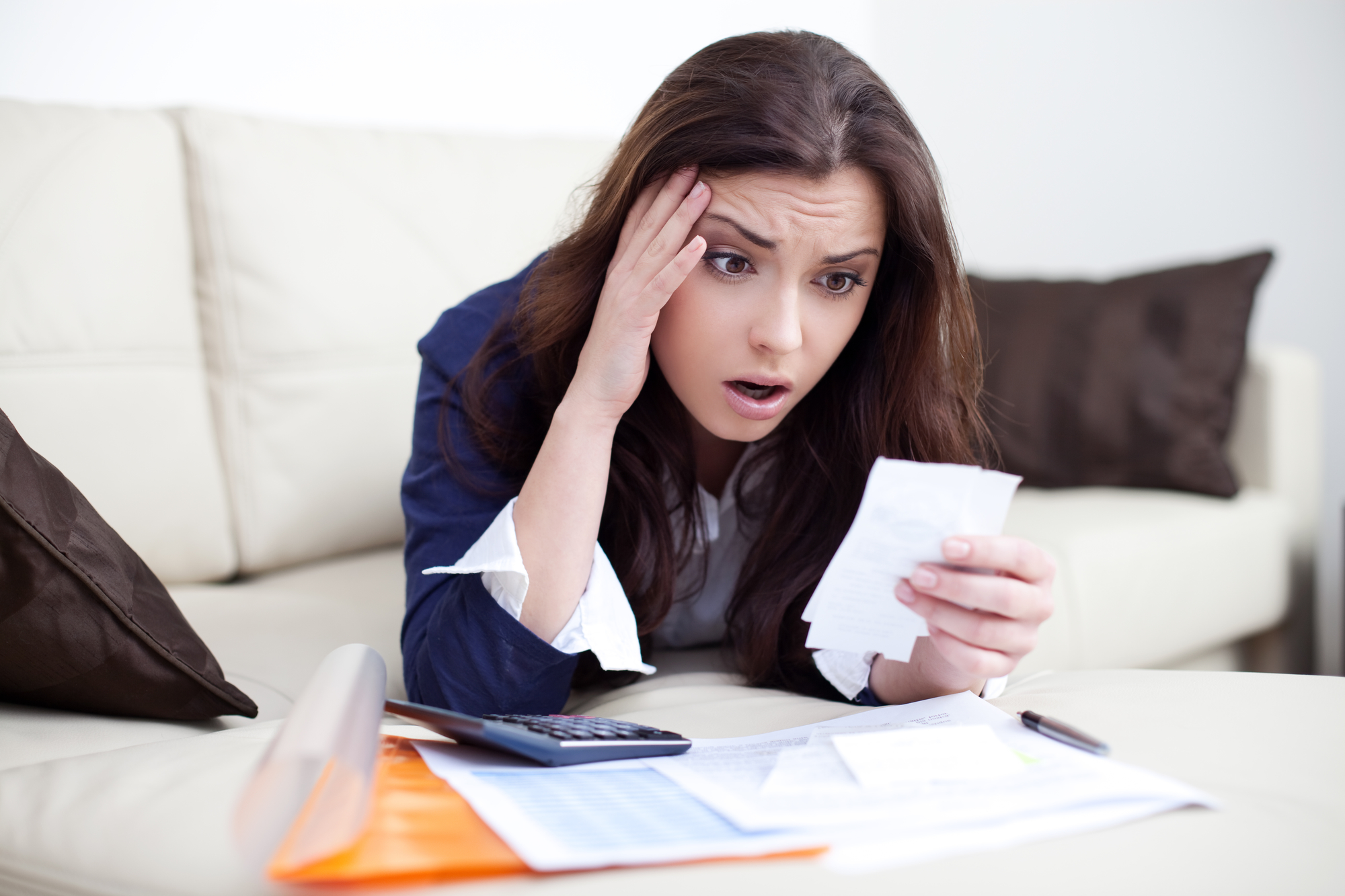 Worried woman looking at bills lying on couch in living room