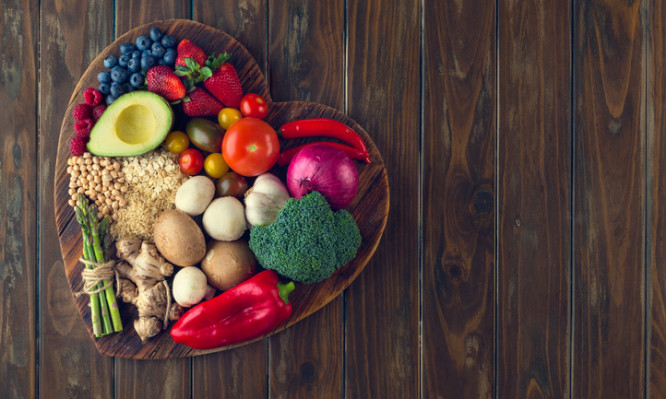 Healthy food on a heart shape cutting board. Love of food concept with fruit, vegetables, grains and high fibre foods. Rustic wood textures