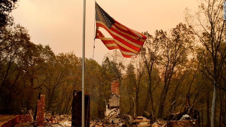 A tattered flag flies over a burned out home at the Camp Fire, Sunday, Nov. 11, 2018, in Paradise, Calif. (AP Photo/John Locher)