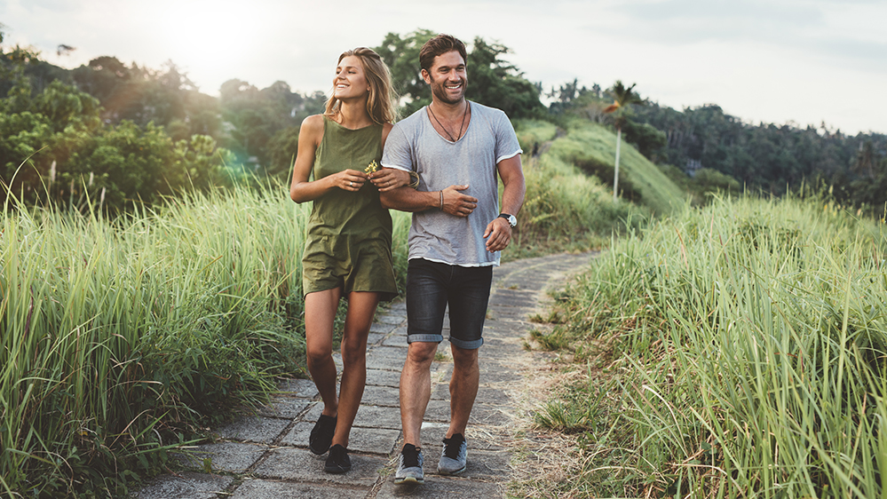 Outdoor shot of young couple in love walking on pathway through grass field. Man and woman walking along tall grass field.