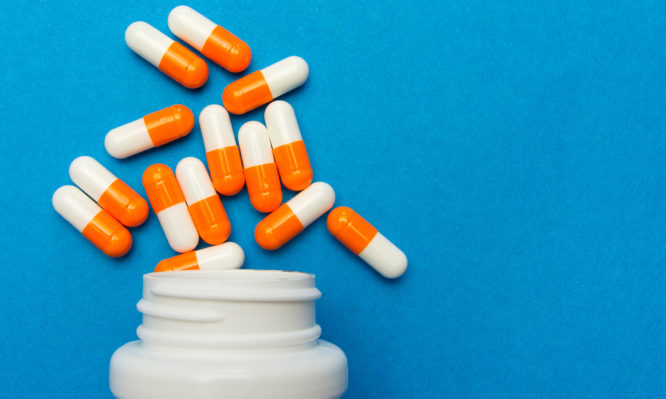 Orange white capsules (pills) were poured from a white bottle on a blue background. Medical background, template.