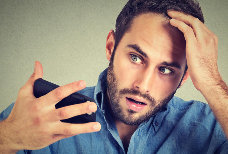 Preoccupied shocked man feeling head, surprised he is losing hair, receding hairline, bad news isolated on gray background. Negative facial expressions, emotion