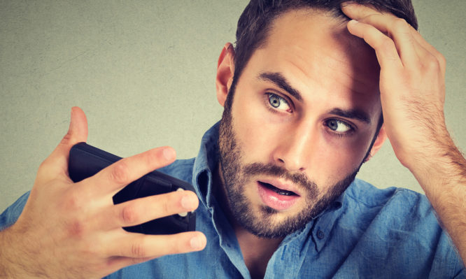 Preoccupied shocked man feeling head, surprised he is losing hair, receding hairline, bad news isolated on gray background. Negative facial expressions, emotion