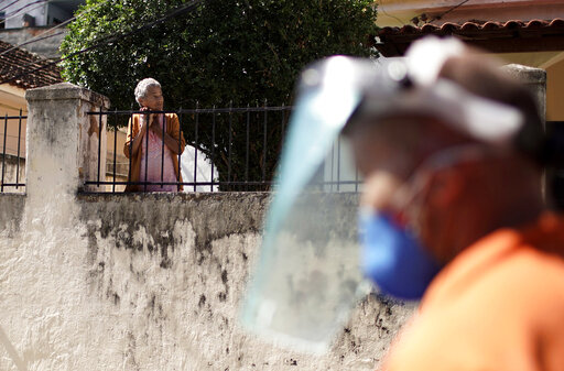 An elderly resident watches a city worker disinfect the Andarai favela as a measure to help curb the spread of the new coronavirus in Rio de Janeiro, Brazil, Monday, April 13, 2020. (AP Photo/Silvia Izquierdo)