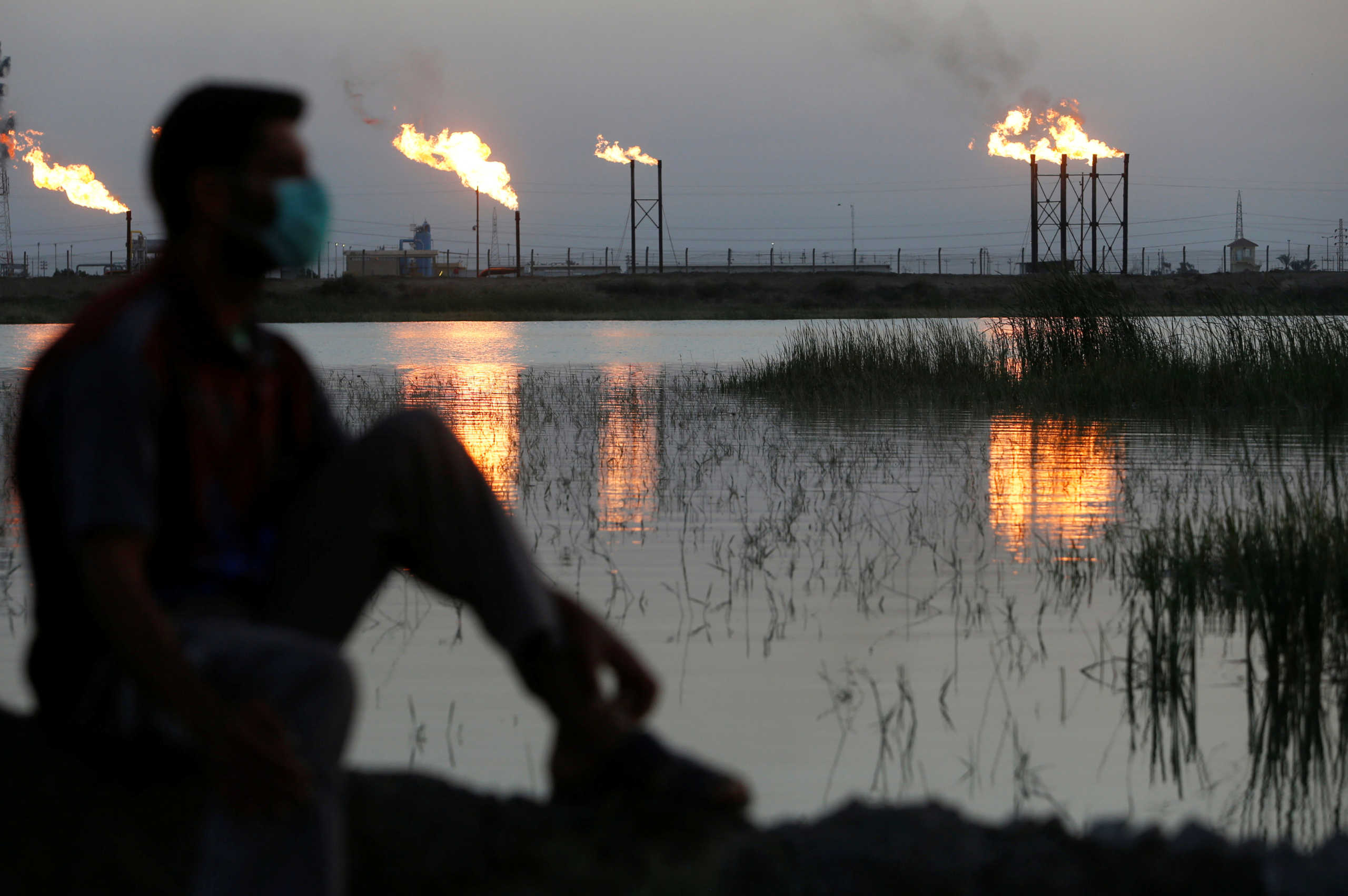 Flames emerge from flare stacks at Nahr Bin Umar oil field, as a man is seen wearing a protective face mask, following the outbreak of the coronavirus, north of Basra, Iraq March 9, 2020. REUTERS/Essam Al-Sudani