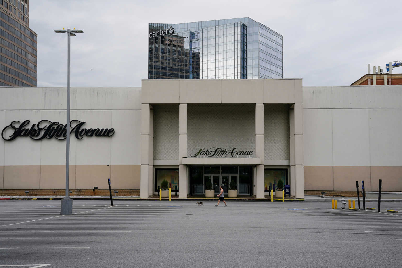 A sman walks a dog in front of a closed Saks Fifth Avenue store days before the phased reopening of businesses and restaurants from coronavirus disease (COVID-19) restrictions in Atlanta, Georgia, U.S. April 22, 2020. REUTERS/Elijah Nouvelage