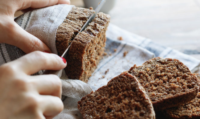 The girl cuts whole-wheat rye bread on a wooden table.