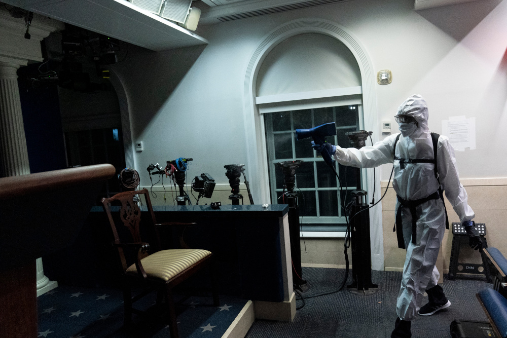 A member of the cleaning staff dressed in a protective suit, sprays the James Brady Briefing Room of the White House, Monday, Oct. 5, 2020, in Washington. (AP Photo/Alex Brandon)