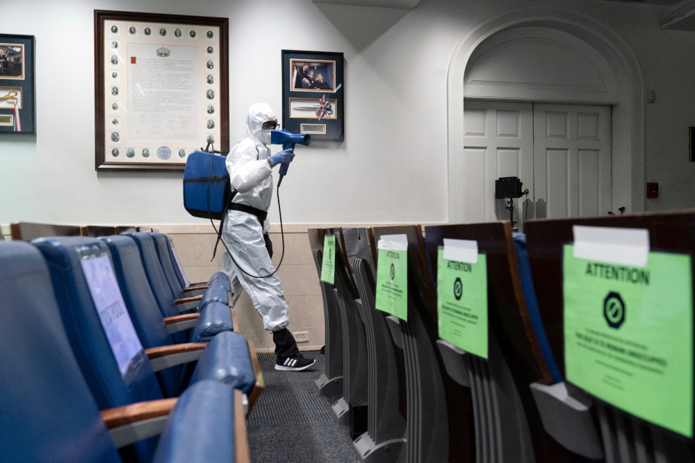 A member of the cleaning staff dressed in a protective suit, sprays the James Brady Briefing Room of the White House, Monday, Oct. 5, 2020, in Washington. (AP Photo/Alex Brandon)