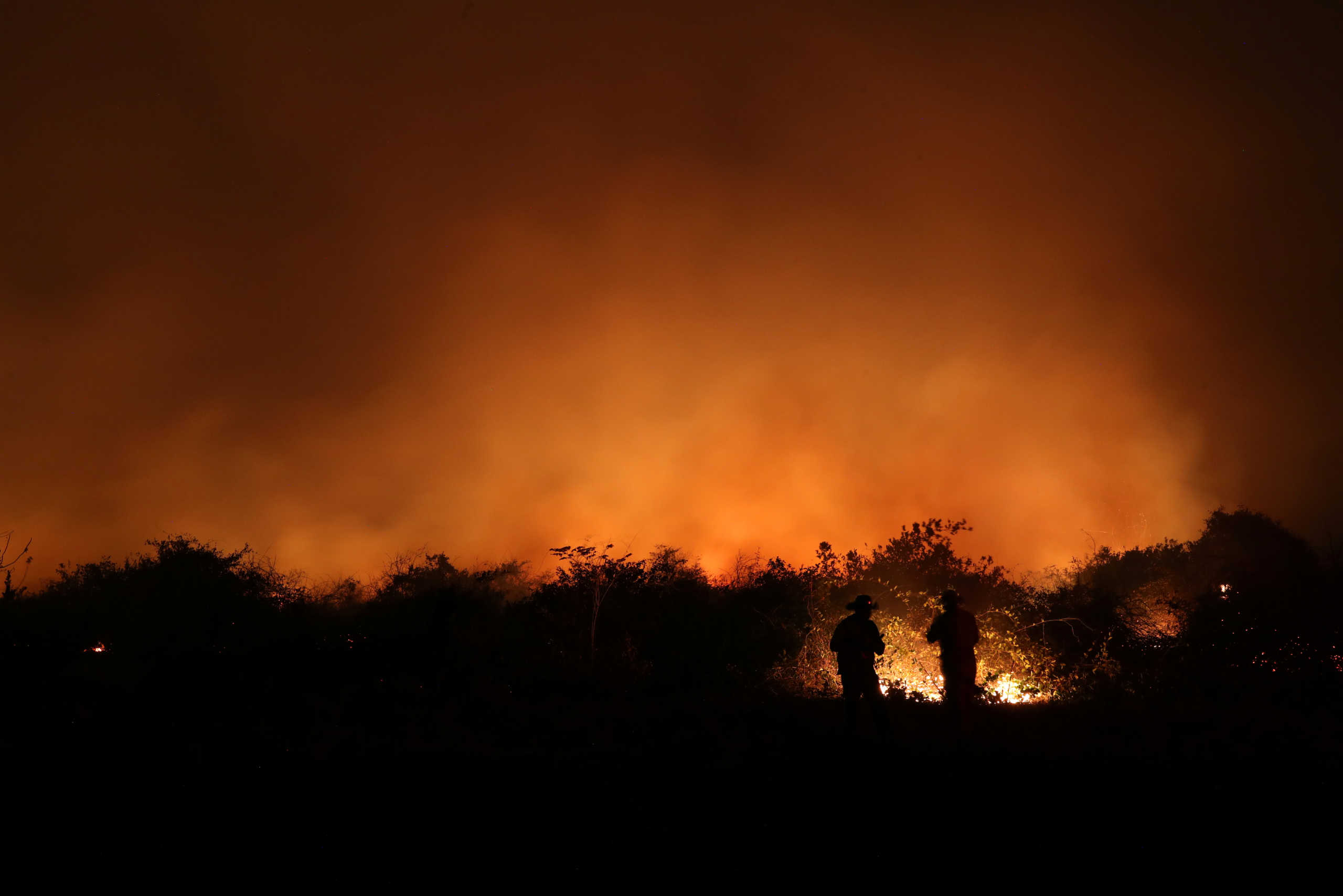 Farm employees stand in front of a burning fire at a ranch in the Pantanal, the world's largest wetland, in Pocone, Mato Grosso state, Brazil, August 26, 2020. REUTERS/Amanda Perobelli  TPX IMAGES OF THE DAY  SEARCH "PANTANAL PEROBELLI" FOR THIS STORY. SEARCH "WIDER IMAGE" FOR ALL STORIES