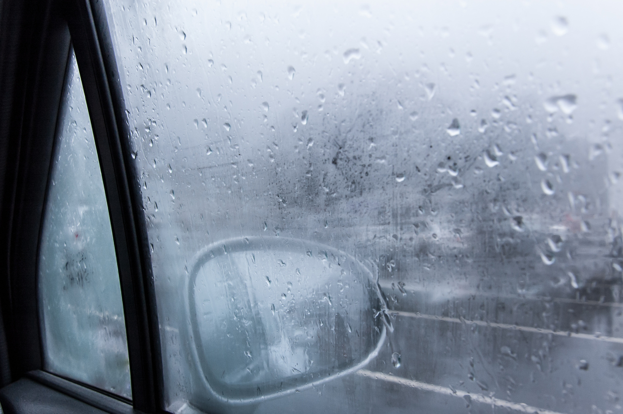 View of a car side mirror from inside the car with condensation and rain on the glass window