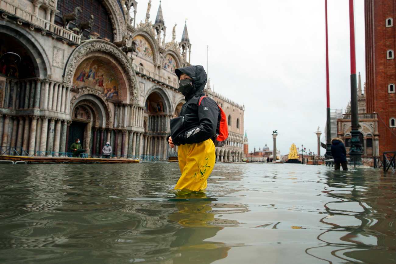 People wade their way through water in flooded St. Mark's Square following a high tide, in Venice, Italy, Tuesday, Dec. 8, 2020. High tides flooded St. Mark’s Square in Venice on Sunday, propelled by winds that were stronger than predicted, so the new system of inflatable barriers wasn’t able to be activated to prevent water from invading the lagoon city. (Anteo Marinoni/LaPresse via AP)