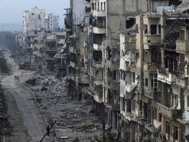 People stand on a street lined with damaged buildings in the besieged area of Homs January 27, 2014. The United States on Monday demanded that Syria allow aid into the "starving" city of Homs, as talks aimed at ending three years of civil war hit more trouble over the future of President Bashar al-Assad. The Syrian government said women and children could leave the besieged city and that rebels should hand over the names of the men who would remain. A U.S. State Department spokesman said an evacuation was not an alternative to immediate aid. REUTERS/Yazan Homsy (SYRIA - Tags: POLITICS CIVIL UNREST CONFLICT)