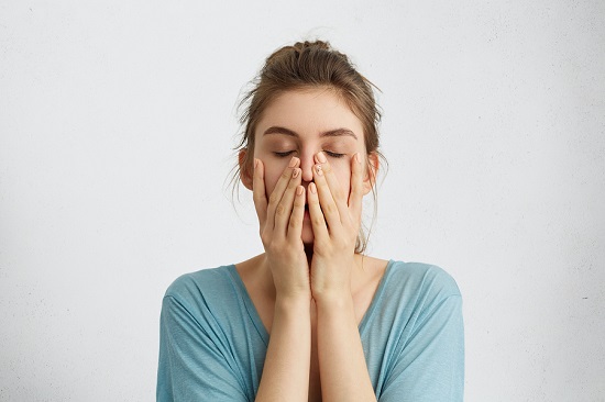 Headshot of young beautiful student female closing her eyes holding hands on chin being tired after hard work trying to relax for a minute and to gather her thoughts. Tiredness feelings concept