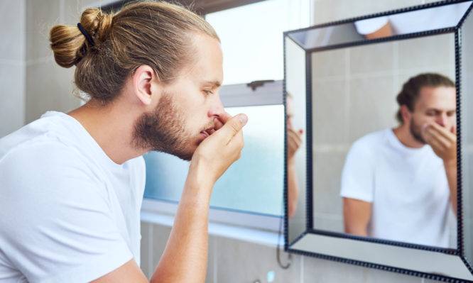 Cropped shot of a young man smelling his breath while standing in his bathroom