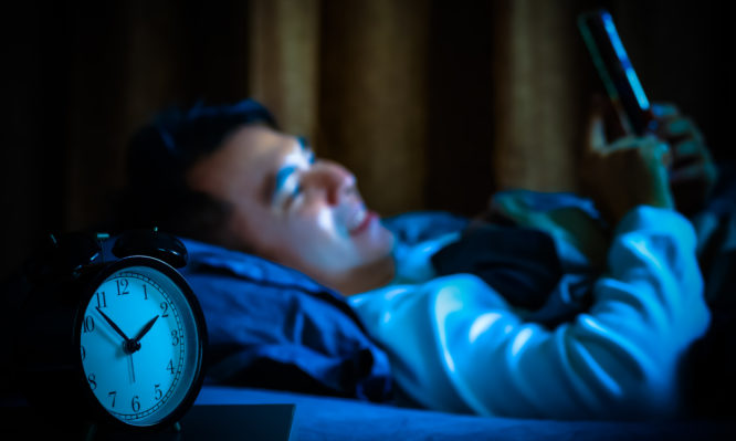 asian man playing social media on smartphone in bed at night causing sleep disorder