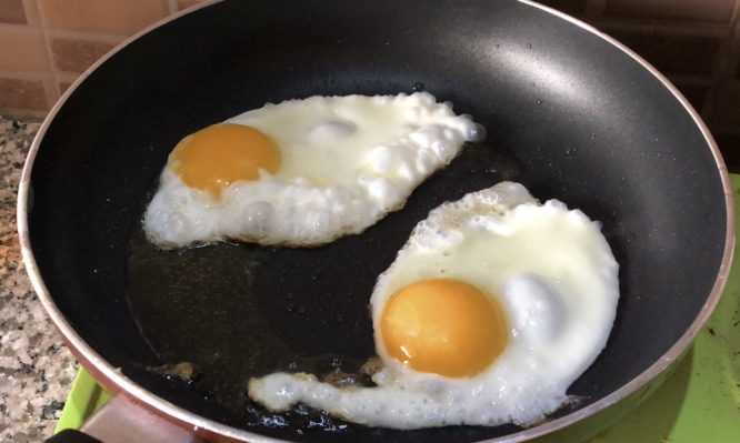 Photo showing two fried eggs that are being cooked in a greasy frying pan, as part of a full-English fried breakfast fry-up.