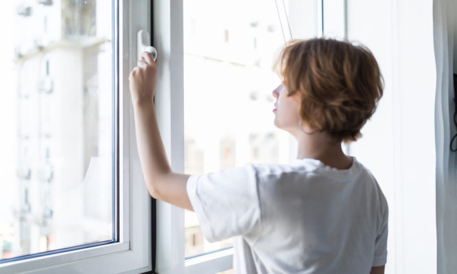 Young woman opening window in living room