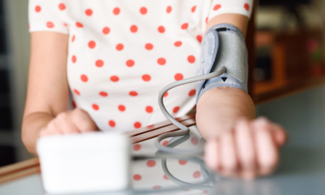 Middle-aged woman measuring her own blood pressure with an electronic blood pressure measurement device at home