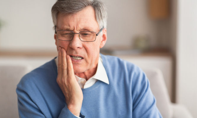 Elderly Man Having Toothache Touching Cheek Suffering From Pain Sitting On Sofa At Home. Selective Focus