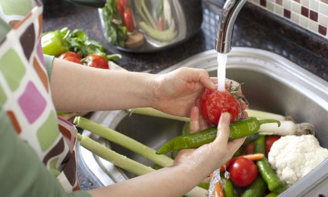 Woman washing vegetables in kitchen close up.