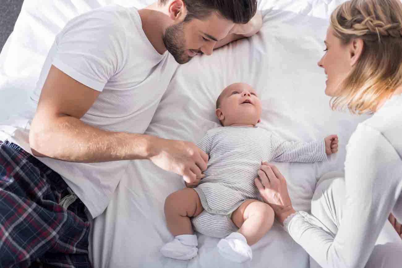 happy parents relaxing with cute baby boy in bed at home