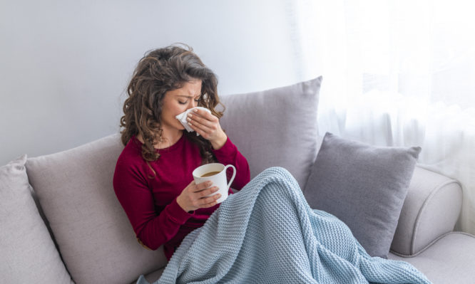 Sick day at home. Asian woman has runny and common cold. Cough. Closeup Of Beautiful Young Woman Caught Cold Or Flu Illness. Portrait Of Unhealthy Girl In Scarf Feeling Pain In Throat.