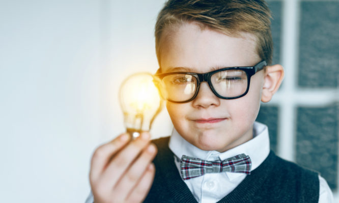 Boy with glasses holds a light bulb in his hand. It lights up: concept of getting a good idea. The boy also wears a bow tie.