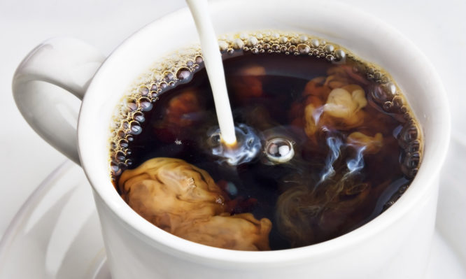 Pouring creamer into a cup of coffee