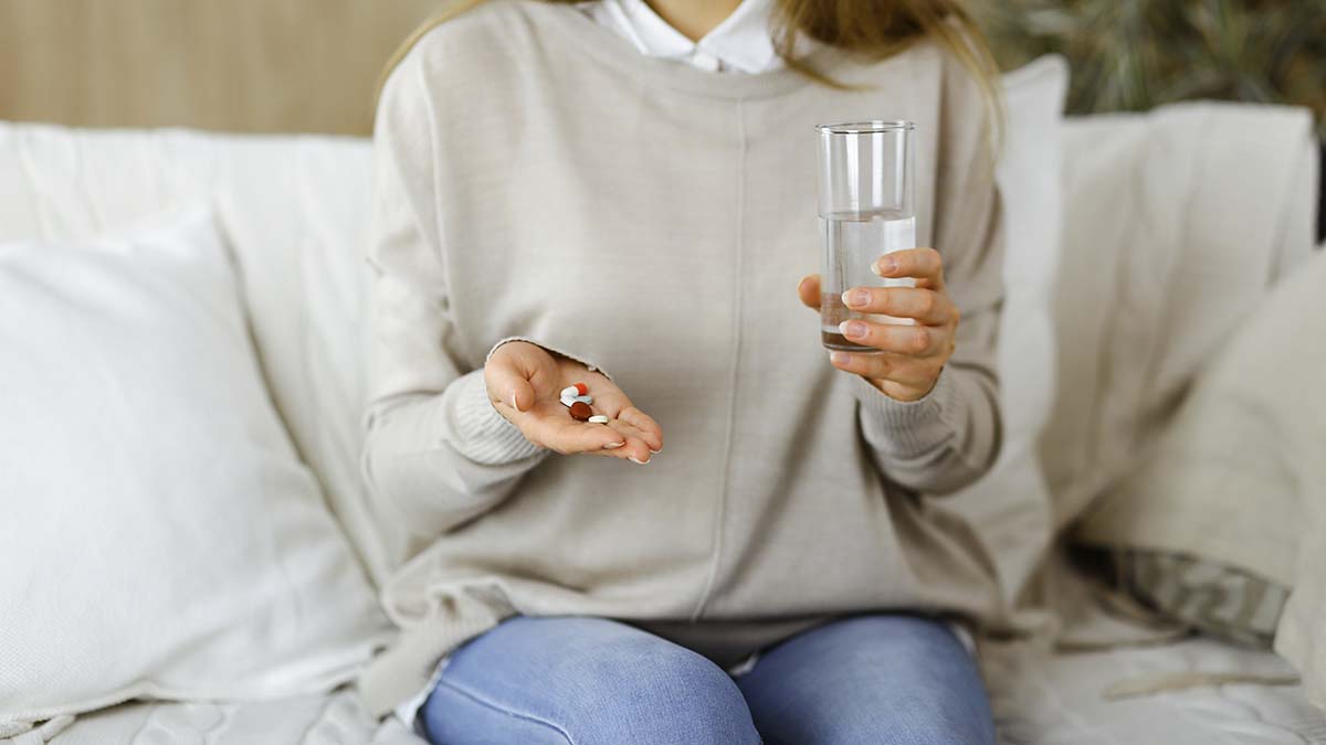 Close-up woman holding pills time to take medications, cure for headache, high blood pressure pain killer drugs at home. Stay at home concept during Coronavirus pandemic.