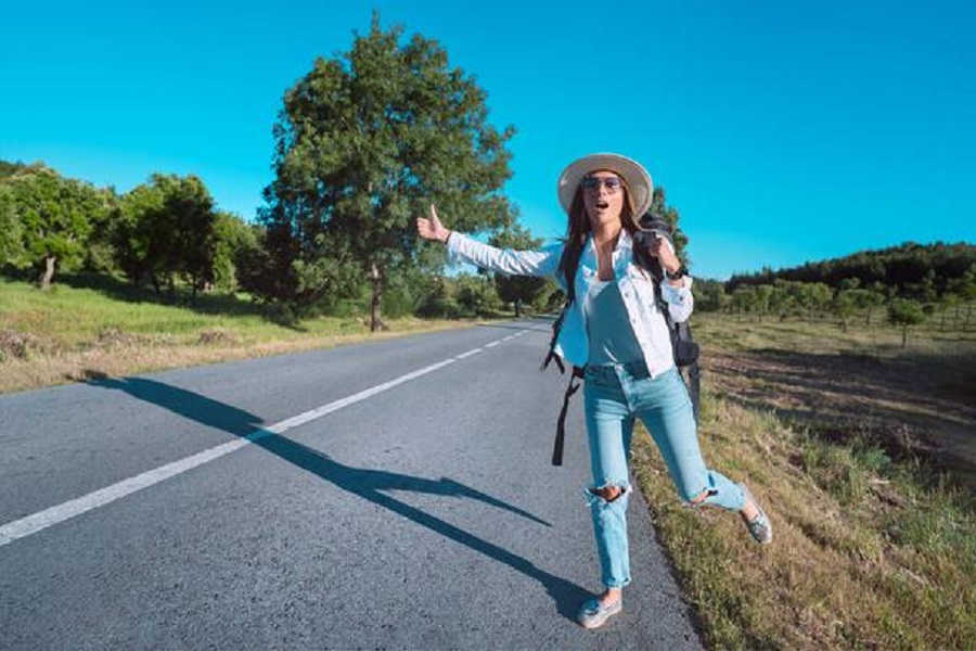 Young attractive woman tourist with backpack hitchhiking on the road. Traveling by autostop. Backpacker stopping car with thumbs up. Picking up hitchhikers. Summer vacation. High quality photo