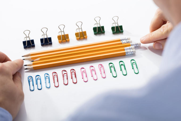 Businessman Arranging The Pencils In Between The Row Of Colorful Pins And Paper Clips