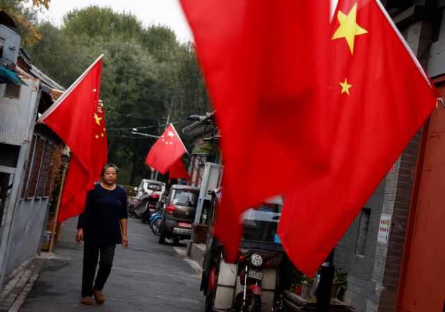 A woman walks through a hutong alley hung with Chinese national flags, ahead of the 20th National Congress of the Communist Party of China, in Beijing, China October 14, 2022. REUTERS/Tingshu Wang