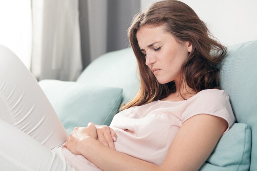 Young woman in pain lying on couch at home, casual style indoor shoot