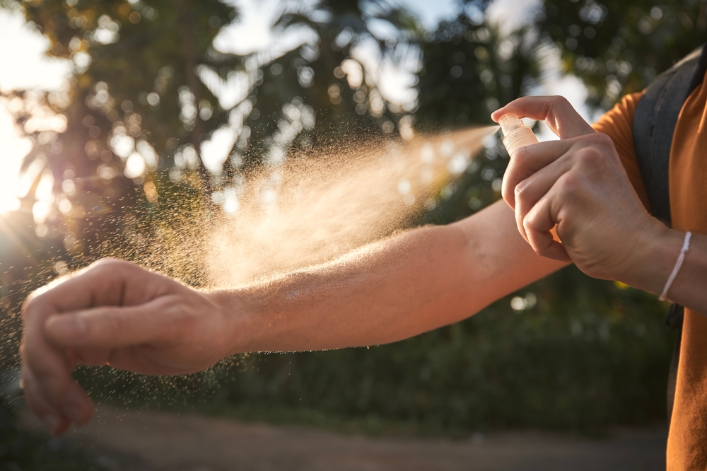 Man is applying insect repellent on his hand against palm trees. Prevention against mosquito bite in tropical destination.