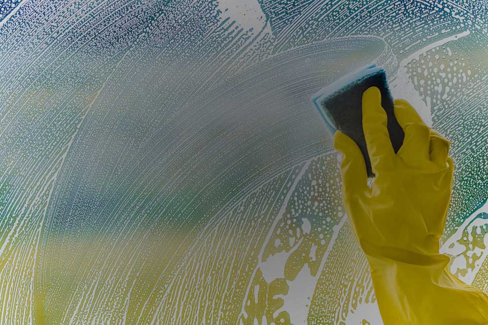 Windows cleaning, smudges or smear on glass made from foam and sponge. Woman washing window with yellow gloves in modern house.